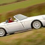 El Jensen S-V8 es una rareza en la historia de los roadsters. Concebido inicialmente con un motor V6, la demanda de los clientes hizo que Jensen equipara el coche con un V8 Ford Mustang de 4.6 litros, proporcionando 329 caballos de fuerza. Con una velocidad máxima de 160 mph y una aceleración de 0 a 60 mph en menos de 5 segundos, el S-V8 era un roadster de alto rendimiento con un diseño que combinaba lo clásico con lo moderno. Aunque la producción se detuvo en 2002 debido a problemas financieros, el Jensen S-V8 sigue siendo un modelo codiciado por los coleccionistas de coches clásicos.