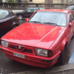 El Alfa Romeo 75 fue uno de los últimos grandes Alfa Romeo tradicionales antes de importantes cambios dentro de la marca italiana. Creado para celebrar el 75 aniversario de Alfa Romeo, destacaba por su agresivo diseño en forma de cuña y una ingeniería muy avanzada para la época. Utilizaba una configuración transaxle con la caja de cambios situada atrás para lograr un reparto de pesos casi perfecto. Las versiones equipadas con el famoso motor V6 Busso se convirtieron rápidamente en auténticos objetos de culto gracias a su sonido inconfundible y carácter puramente italiano.